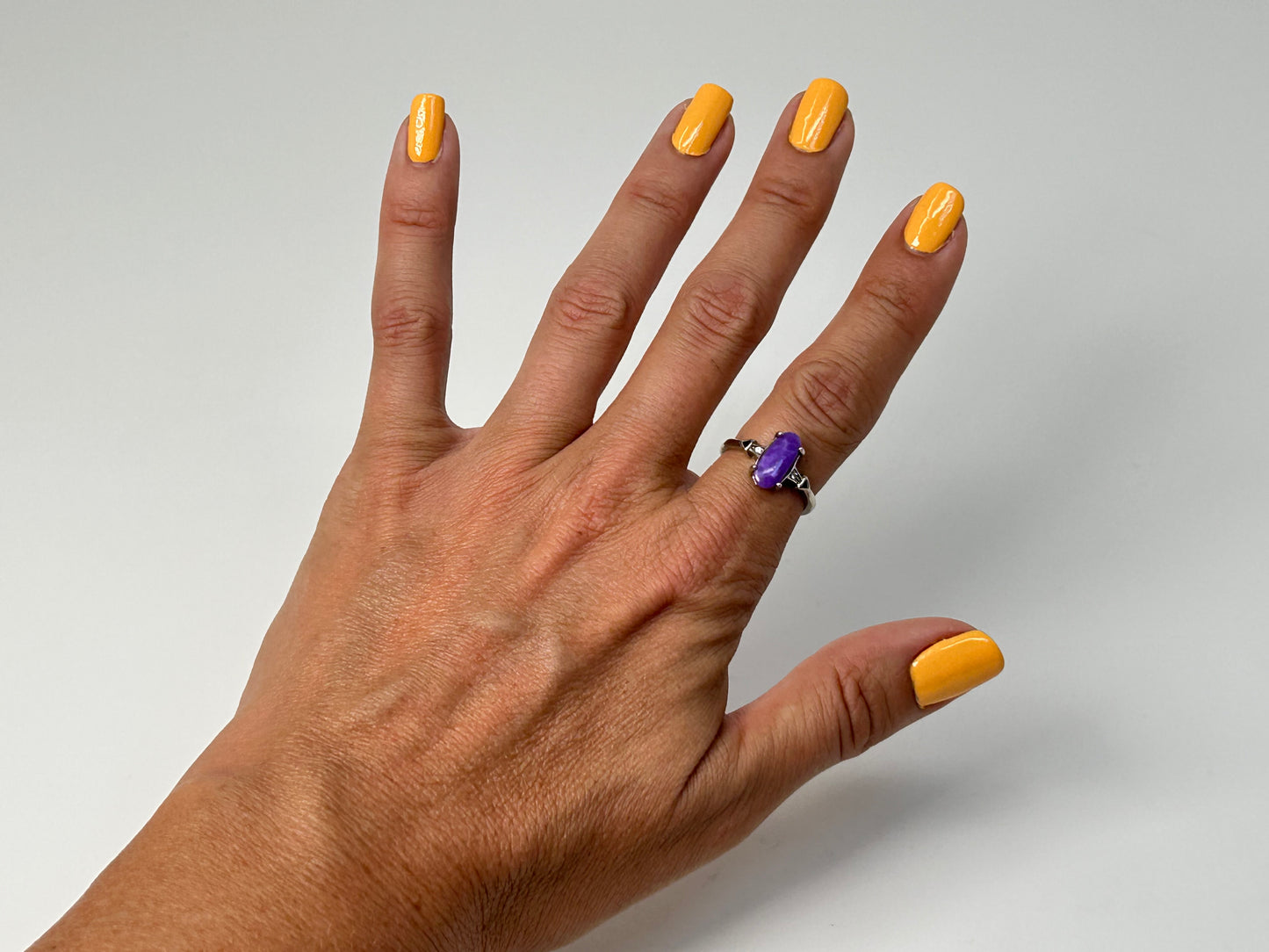 Finger wearing a Purple Sugilite Crystal in Sterling Silver Ring with Cubic Zirconia for natural grounding crystal healing stone with white gray background