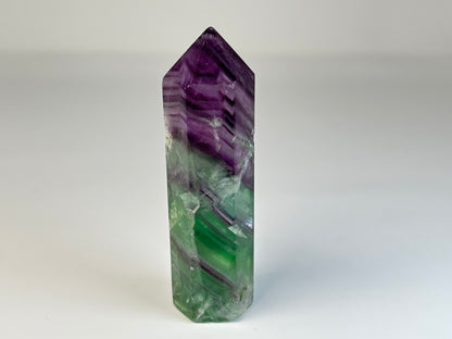 Rainbow Fluorite Tower gemstone on table stand with white background.