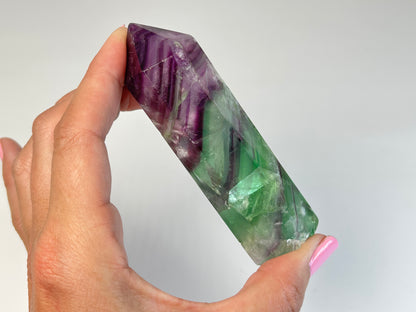 Hand holding a Rainbow Fluorite Tower gemstone with white background.