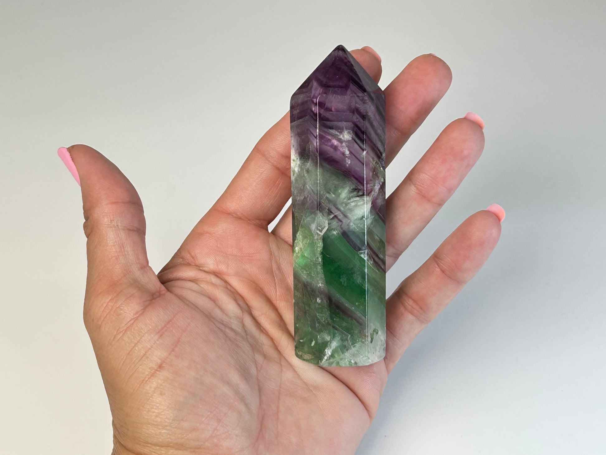 Hand holding a Rainbow Fluorite Tower gemstone for meditation and energy work with white background