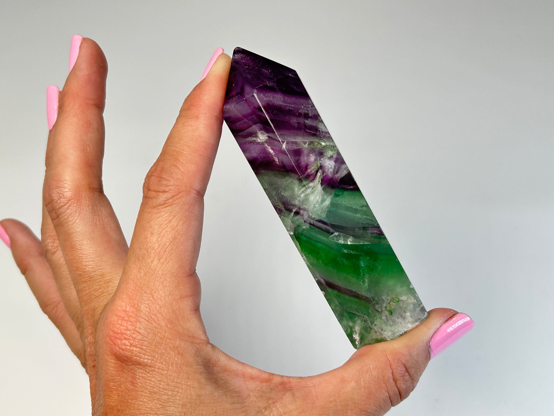 Hand holding a Rainbow Fluorite Tower gemstone on table top with gray  background