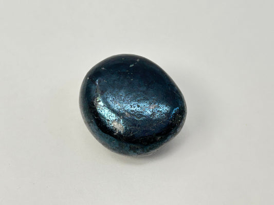 A polished dark blue teardrop-shaped Rare Covellite Healing Stone with a metallic, iridescent sheen, photographed on a neutral light gray background.