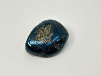 A polished dark blue Rare Healing Covellite Stone with metallic gold and silver mineral inclusions on a plain light gray background.