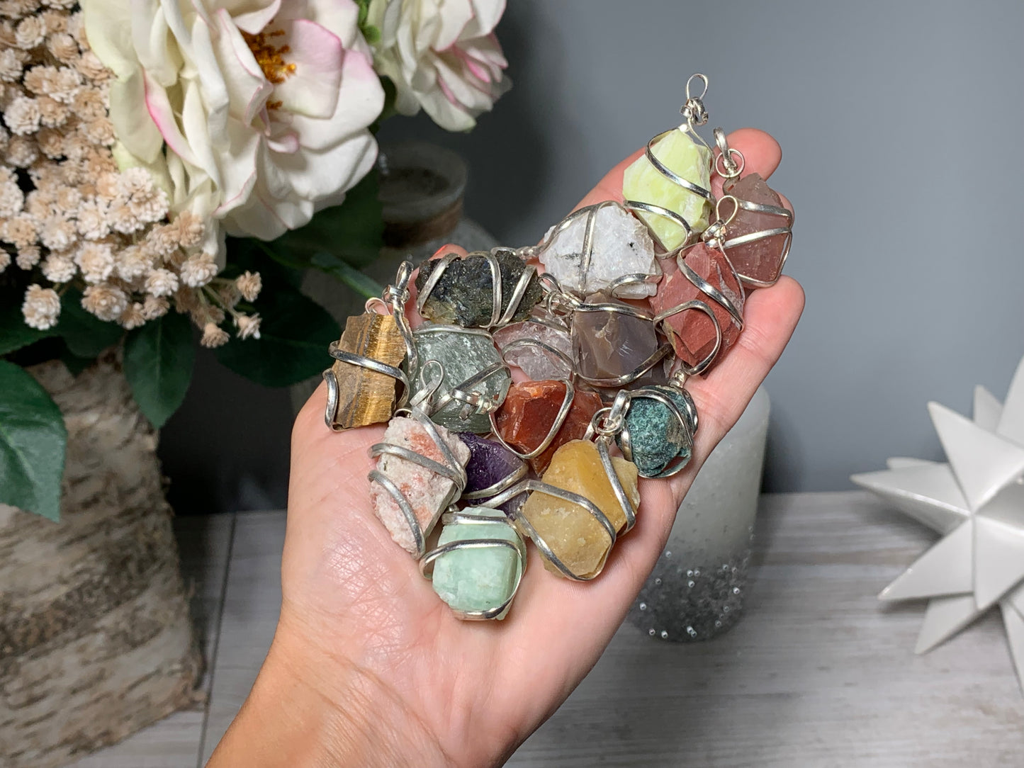 Hand holding Raw Crystal Pendants That Call to You for meditation and energy work with floral background