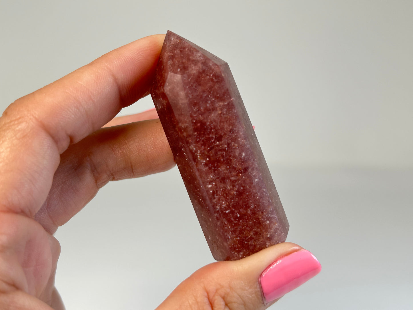 Hand holding a Red Aventurine Crystal Tower for meditation and energy work with white gray background