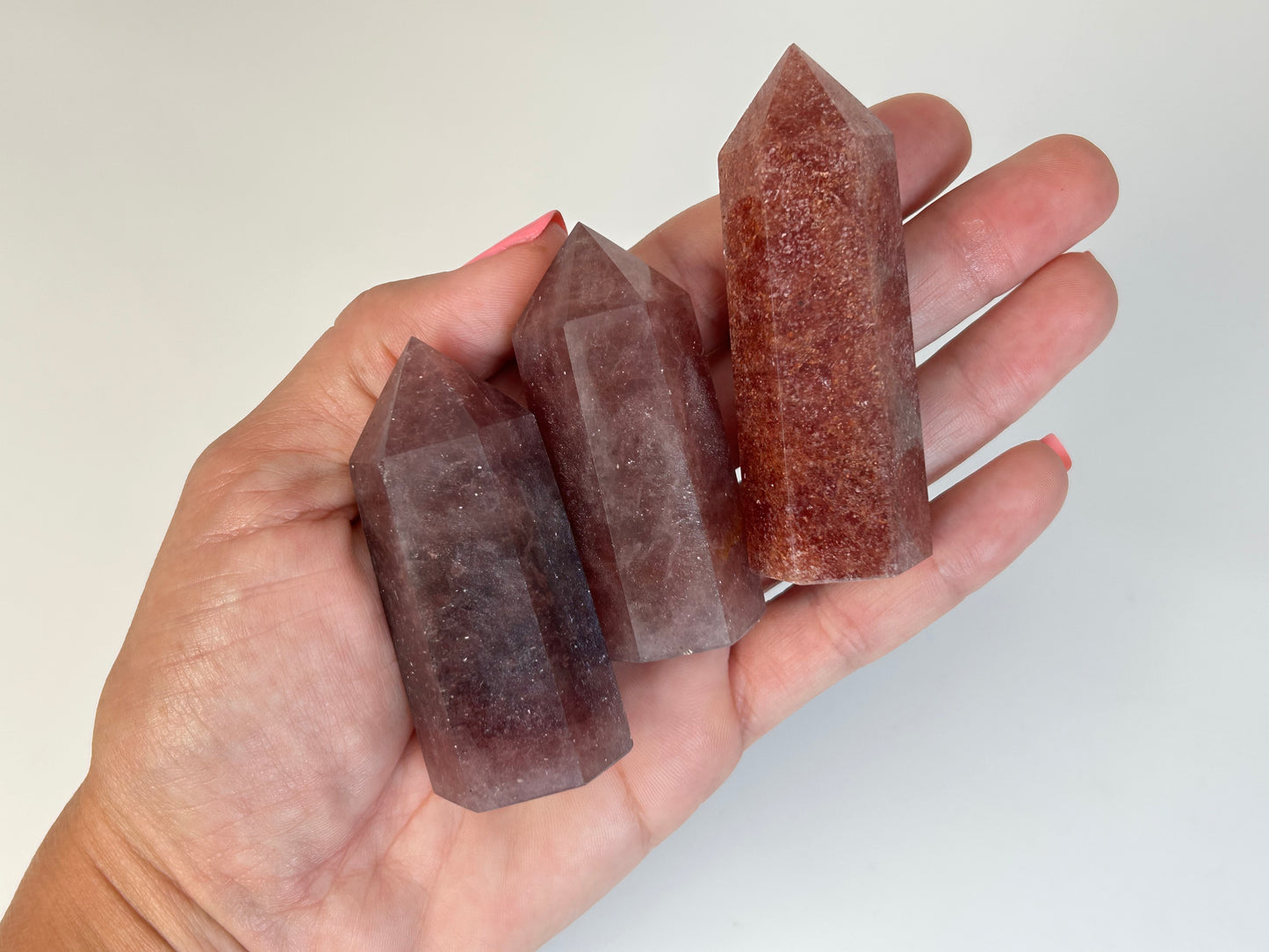 Hand holding three Red Aventurine Crystal Towers against a white background