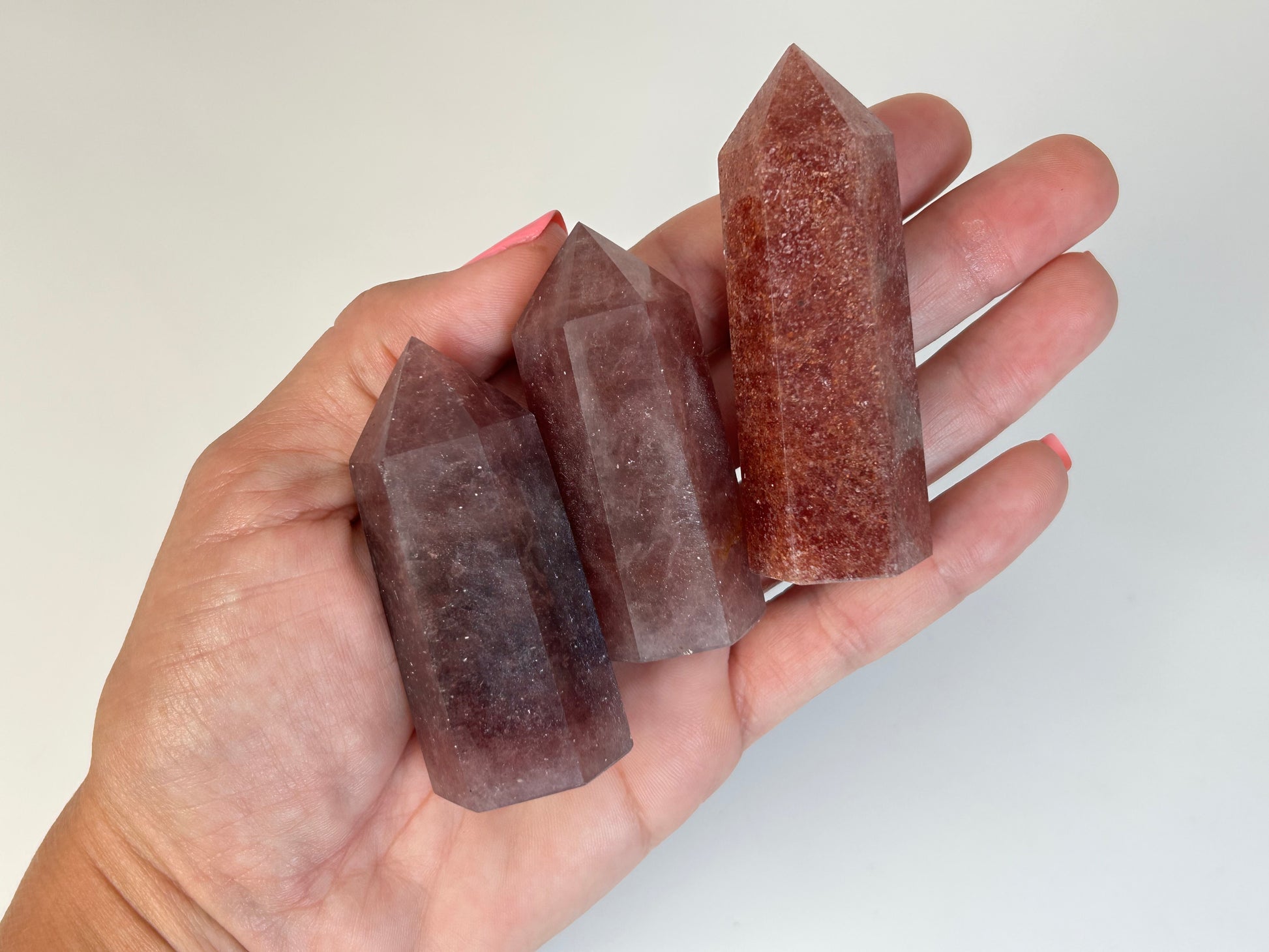 Hand holding three Red Aventurine Crystal Towers against a white background