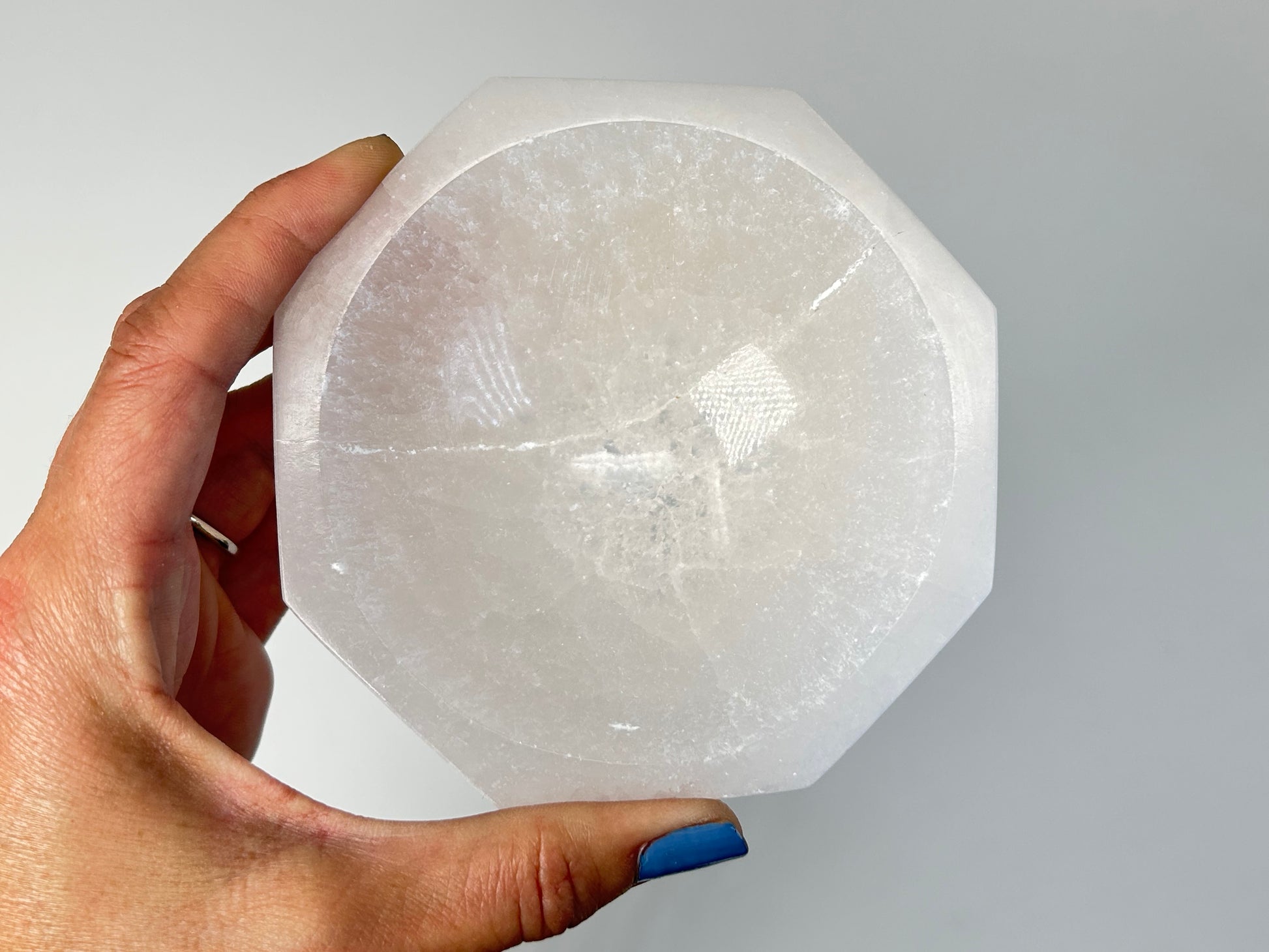 Hand holding a Octagon Selenite Bowl from Morocco for meditation and energy work with white background