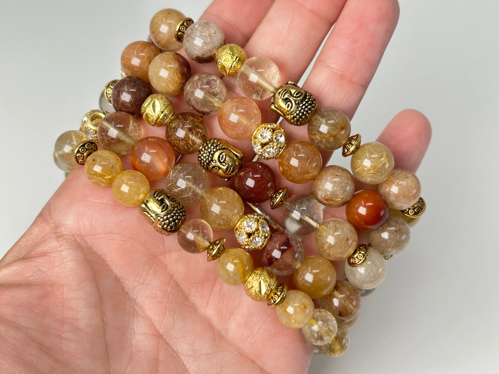 Hand holding Rutile Quartz Bracelets for natural grounding beaded bracelets with gold accents on a light background