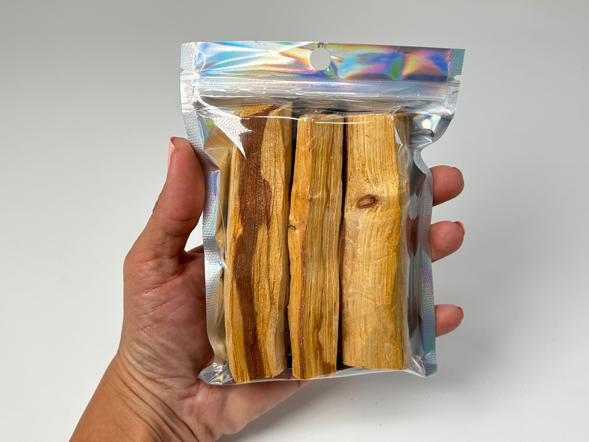 Hand holding Sacred Wood Palo Santo Sticks for meditation and energy work with white background.