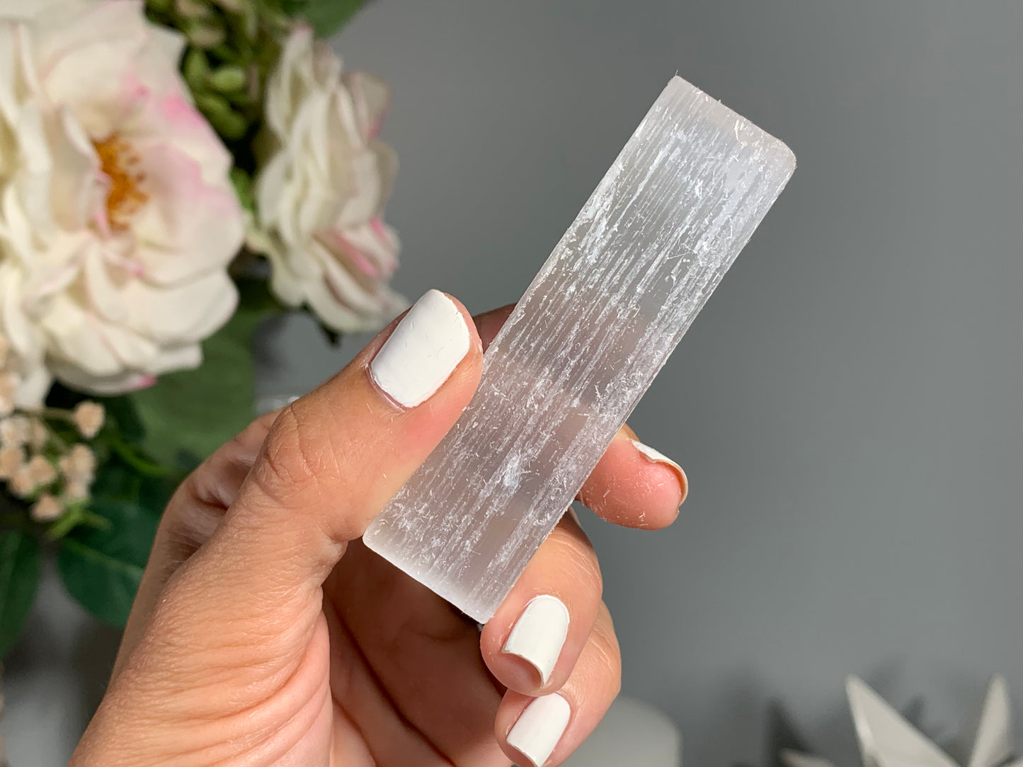 hand holding a Selenite Crystal Cleansing Stick to Purify and Protect for energy and trust with white gray floral background.