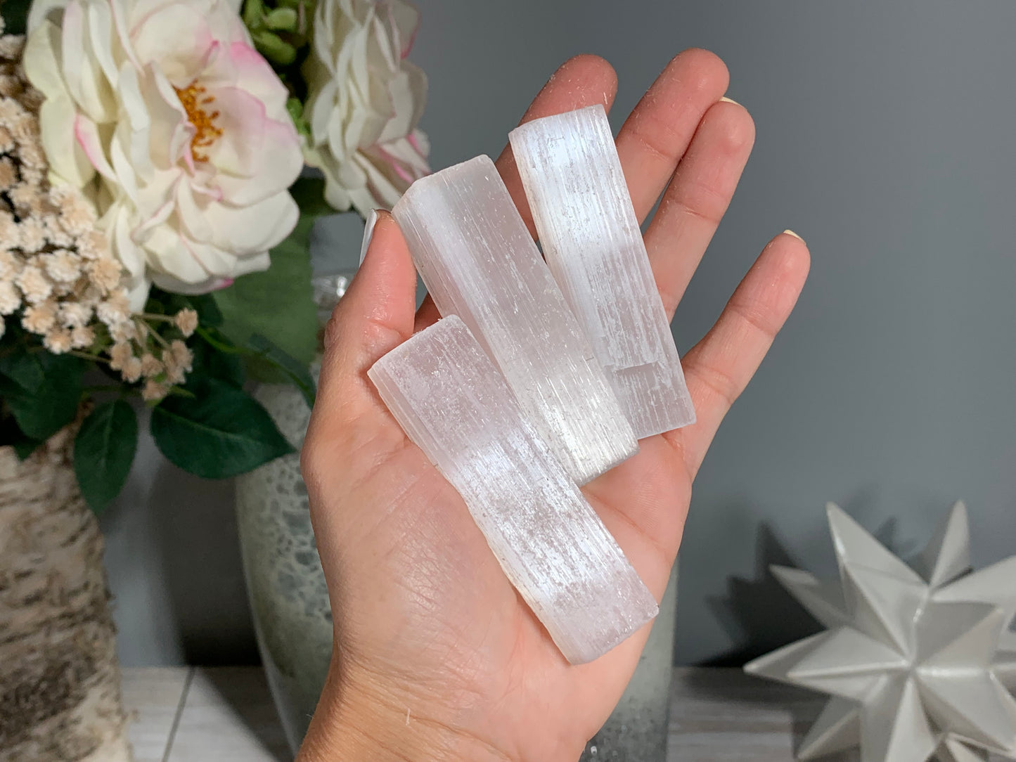 hand holding a Selenite Crystal Cleansing Sticks to Purify and Protect for energy and trust with white gray floral background.