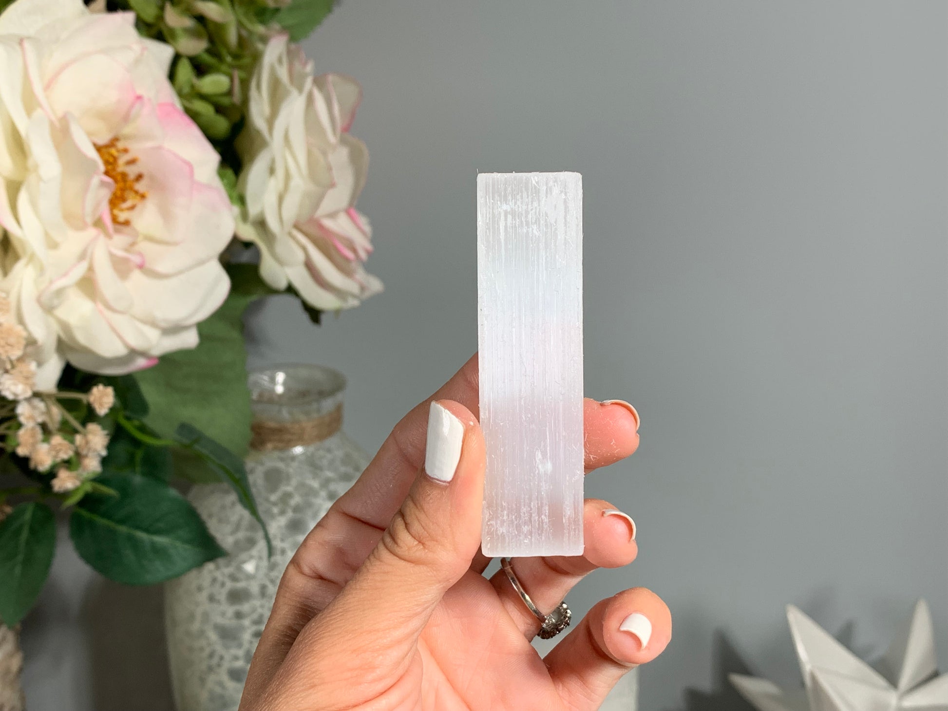 hand holding a Selenite Crystal Cleansing Stick to Purify and Protect for energy and trust with white gray floral background.