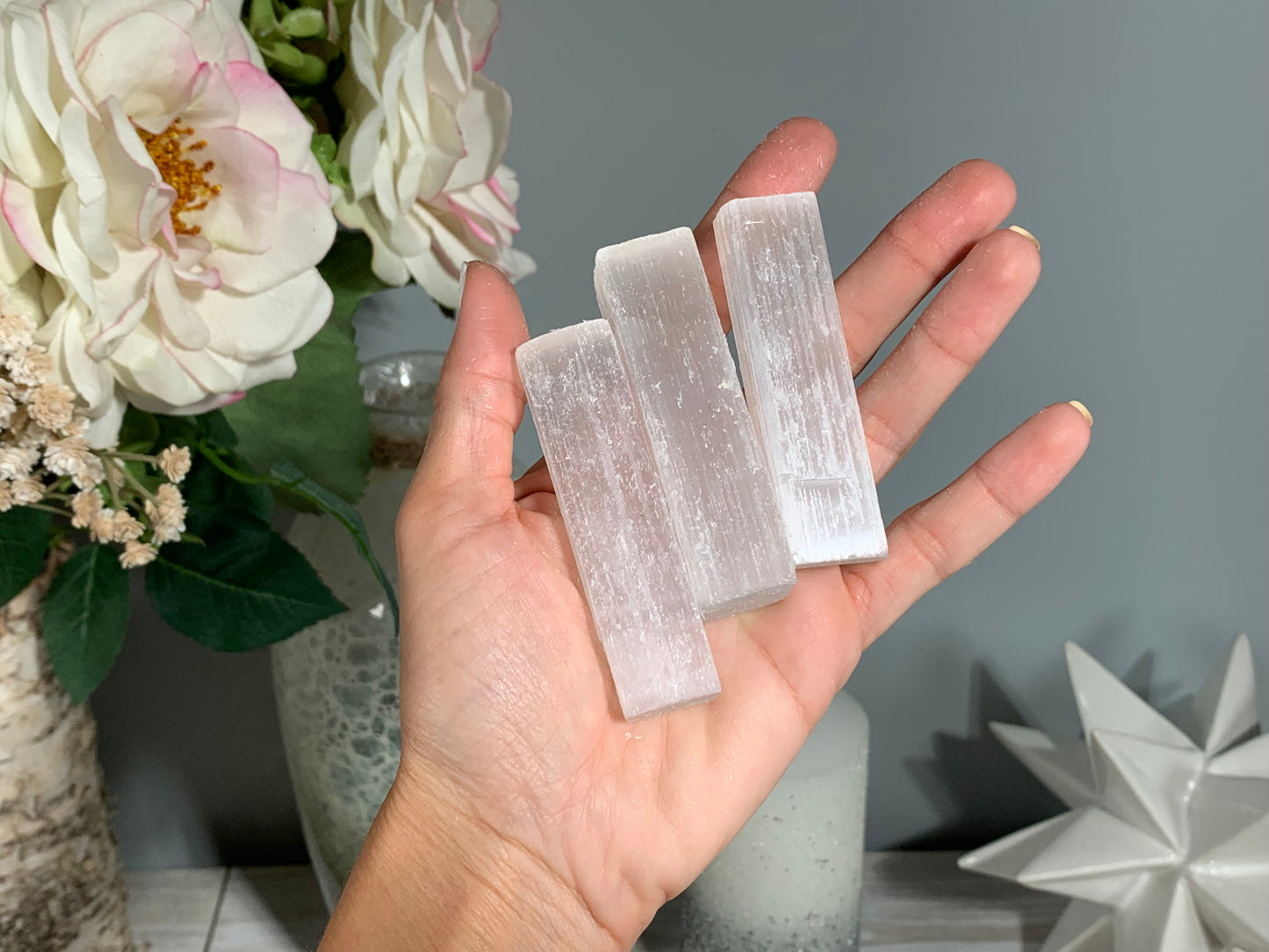 hand holding a Selenite Crystal Cleansing Sticks to Purify and Protect for energy and trust with white gray floral background.