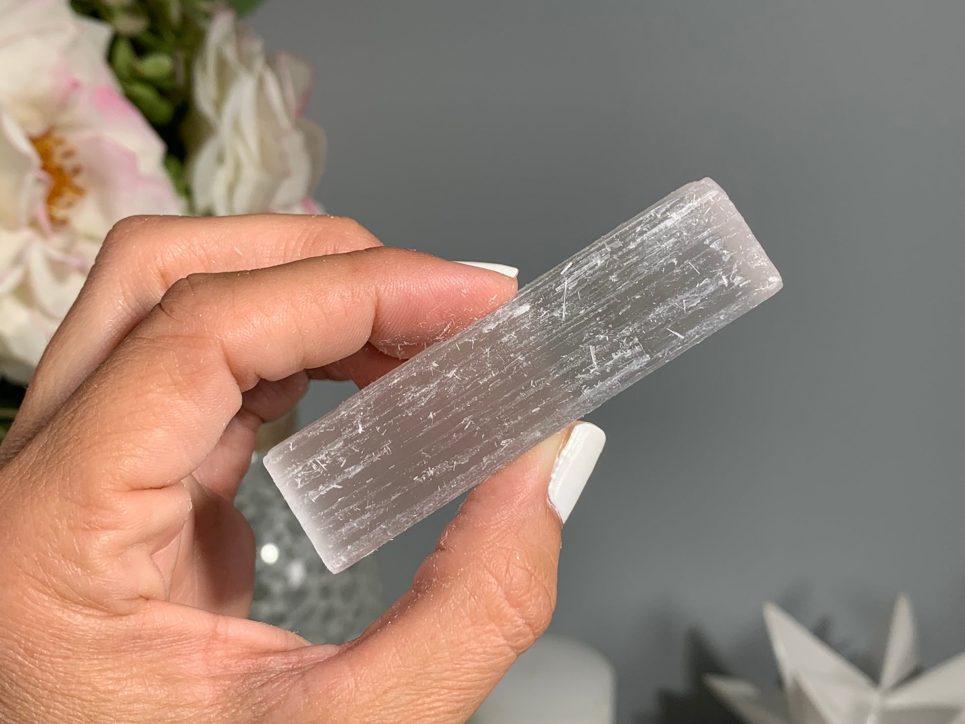hand holding a Selenite Crystal Cleansing Stick to Purify and Protect for energy and trust with white gray floral background.