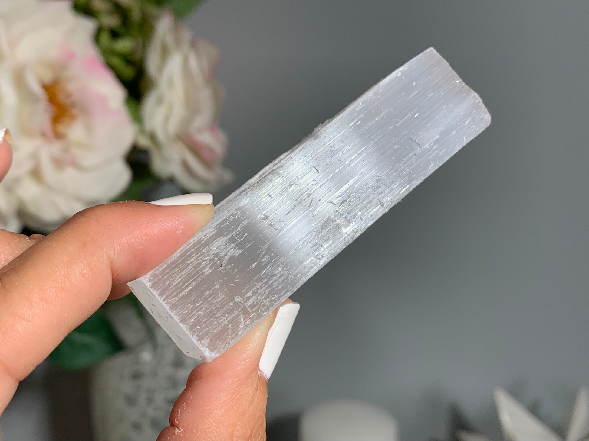 hand holding a Selenite Crystal Cleansing Stick to Purify and Protect for energy and trust with white gray floral background.