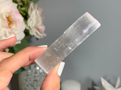 hand holding a Selenite Crystal Cleansing Stick to Purify and Protect for energy and trust with white gray floral background.