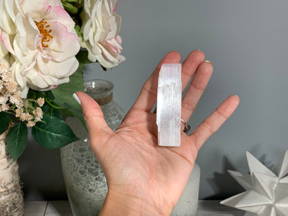 hand holding a Selenite Crystal Cleansing Stick to Purify and Protect for energy and trust with white gray floral background.