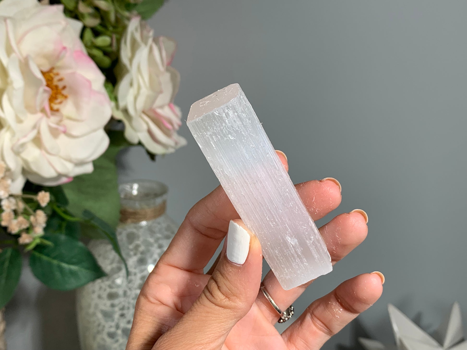 hand holding a Selenite Crystal Cleansing Stick to Purify and Protect for energy and trust with white gray floral background.