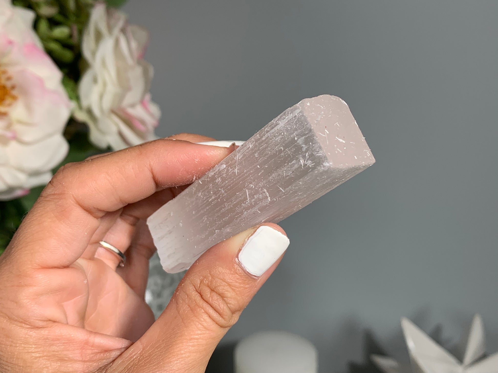 hand holding a Selenite Crystal Cleansing Stick to Purify and Protect for energy and trust with white gray floral background.