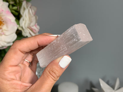 hand holding a Selenite Crystal Cleansing Stick to Purify and Protect for energy and trust with white gray floral background.