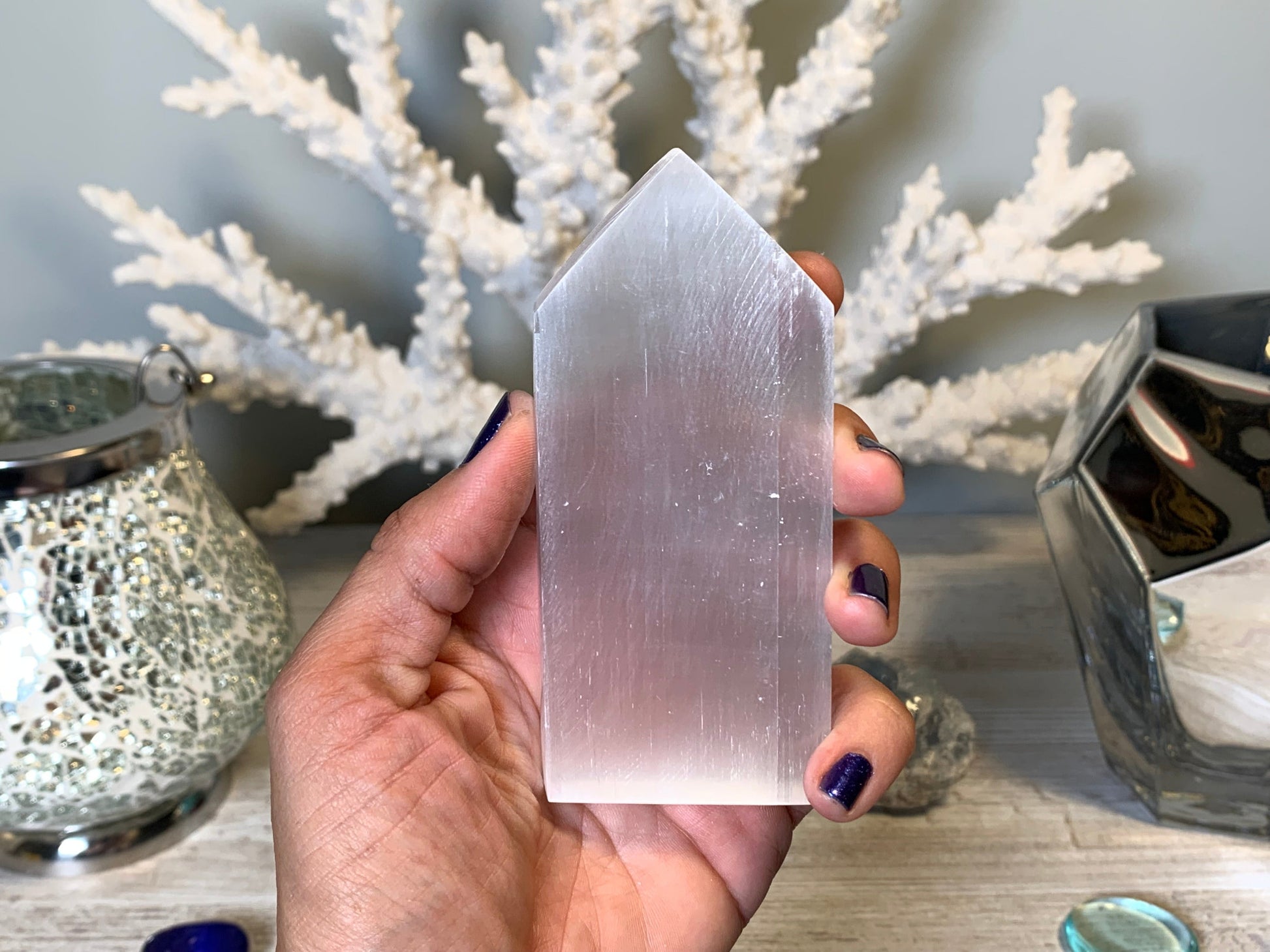 hand holding Selenite Flat Point Crystals for energy and trust with white gray floral background.