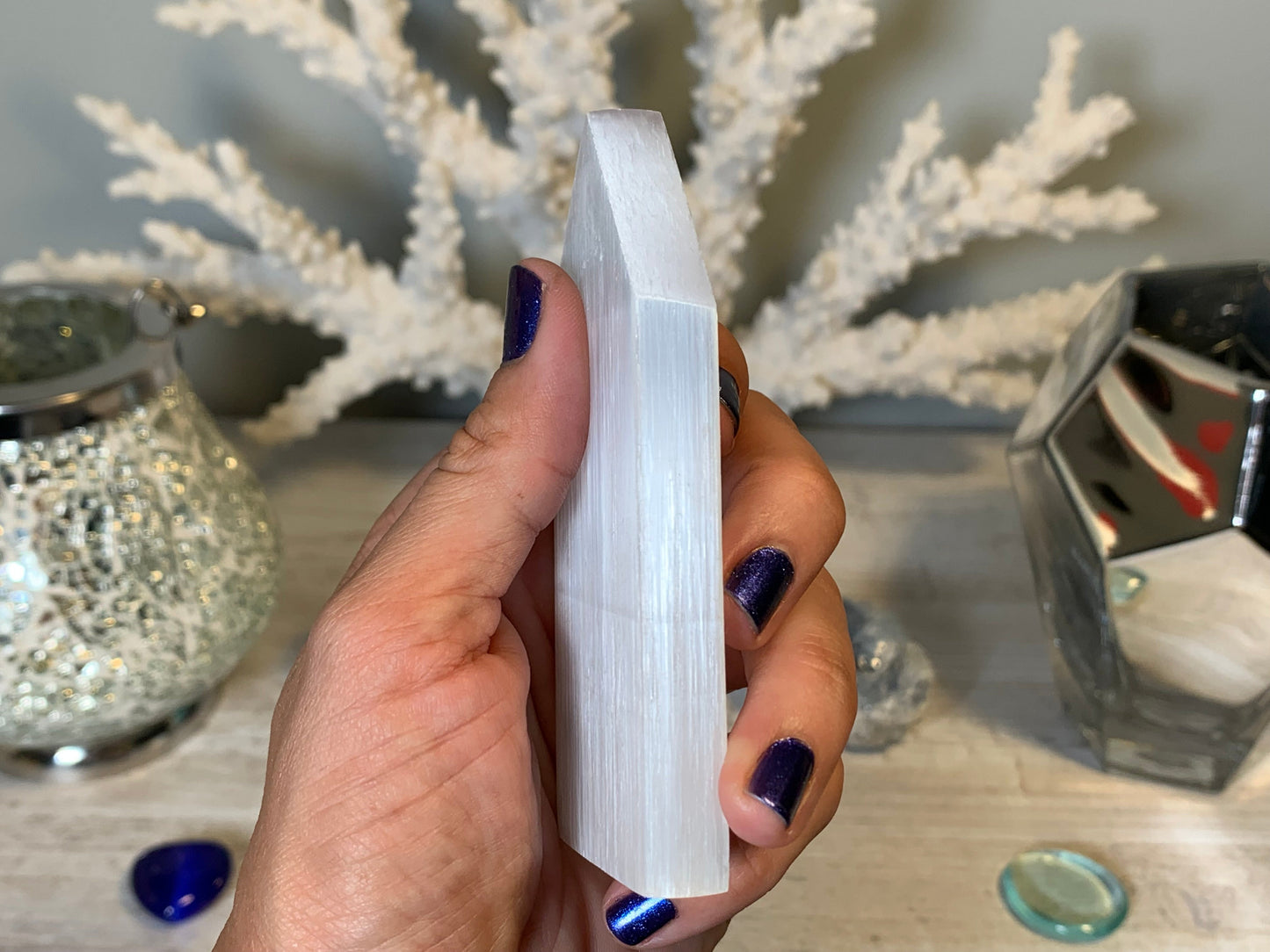 hand holding Selenite Flat Point Crystals for energy and trust with white gray floral background.