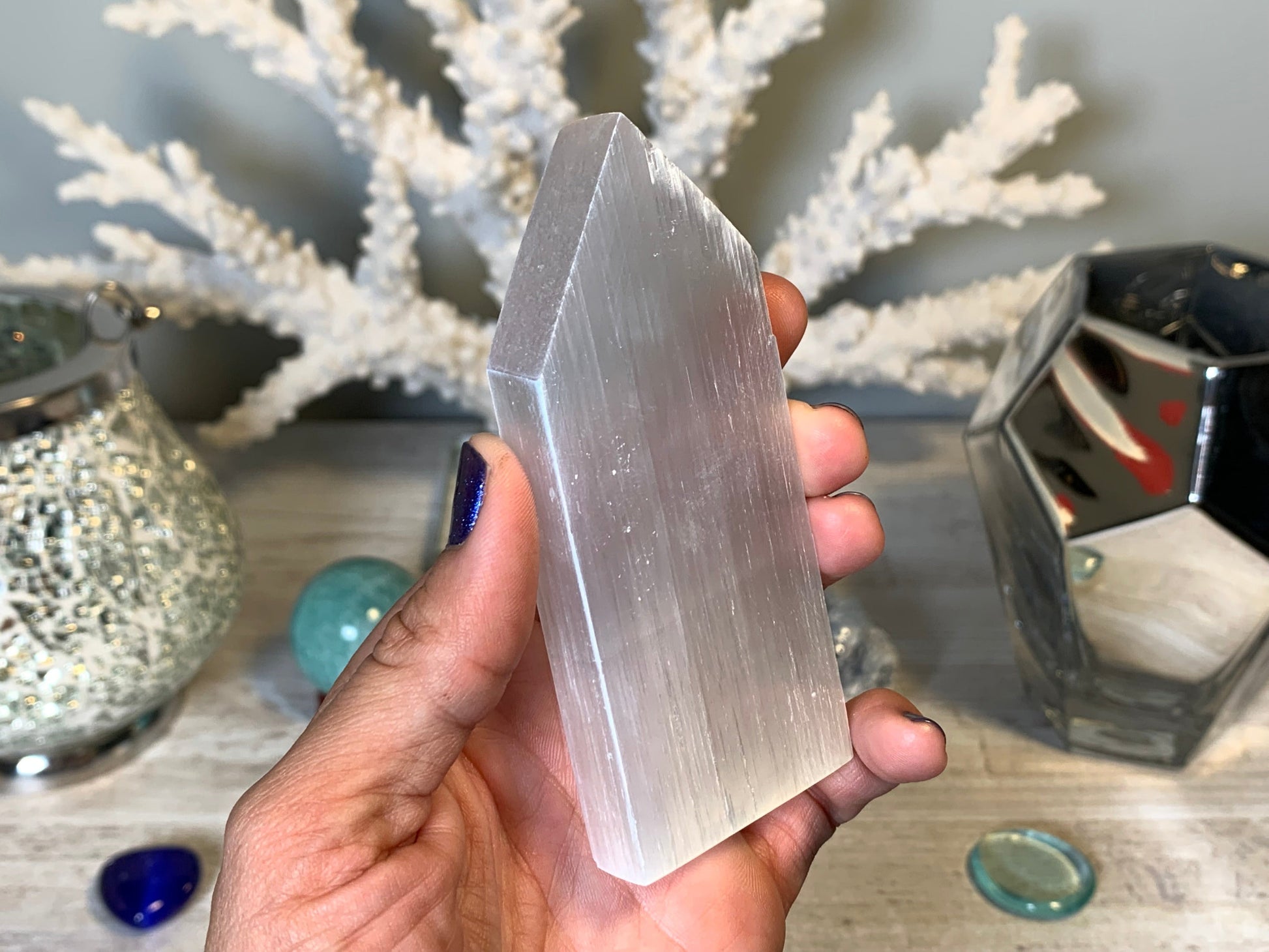 hand holding Selenite Flat Point Crystals for energy and trust with white gray floral background.