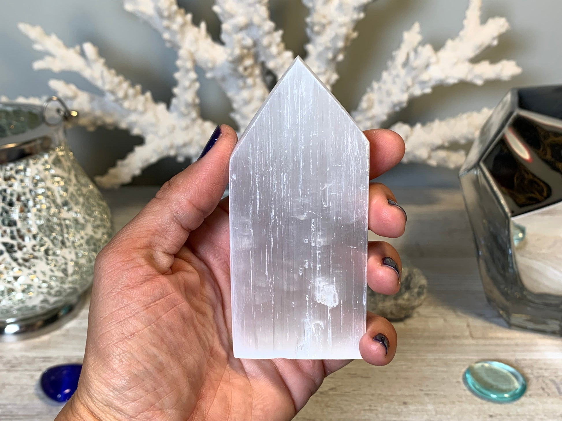 hand holding Selenite Flat Point Crystals for energy and trust with white gray floral background.