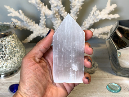 hand holding Selenite Flat Point Crystals for energy and trust with white gray floral background.