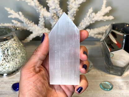 hand holding Selenite Flat Point Crystals for energy and trust with white gray floral background.