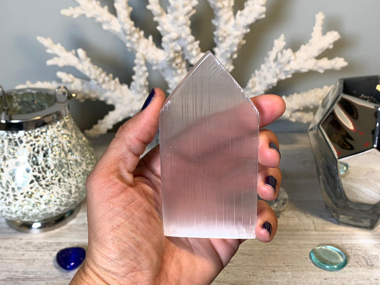 hand holding Selenite Flat Point Crystals for energy and trust with white gray floral background.