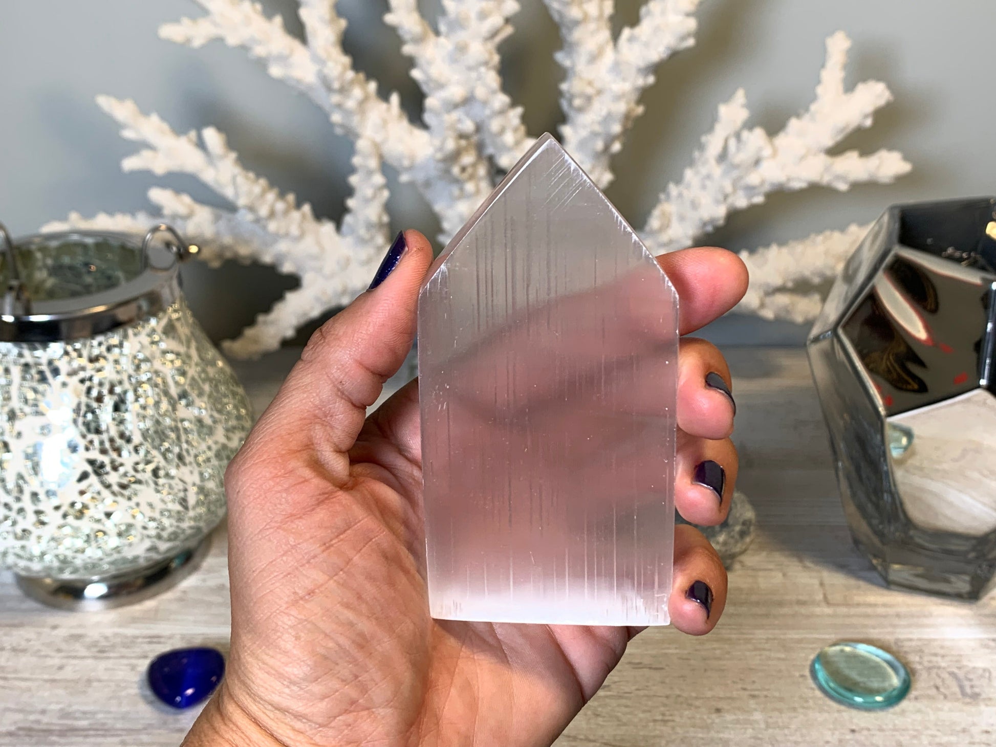 hand holding Selenite Flat Point Crystals for energy and trust with white gray floral background.