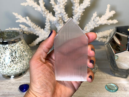 hand holding Selenite Flat Point Crystals for energy and trust with white gray floral background.