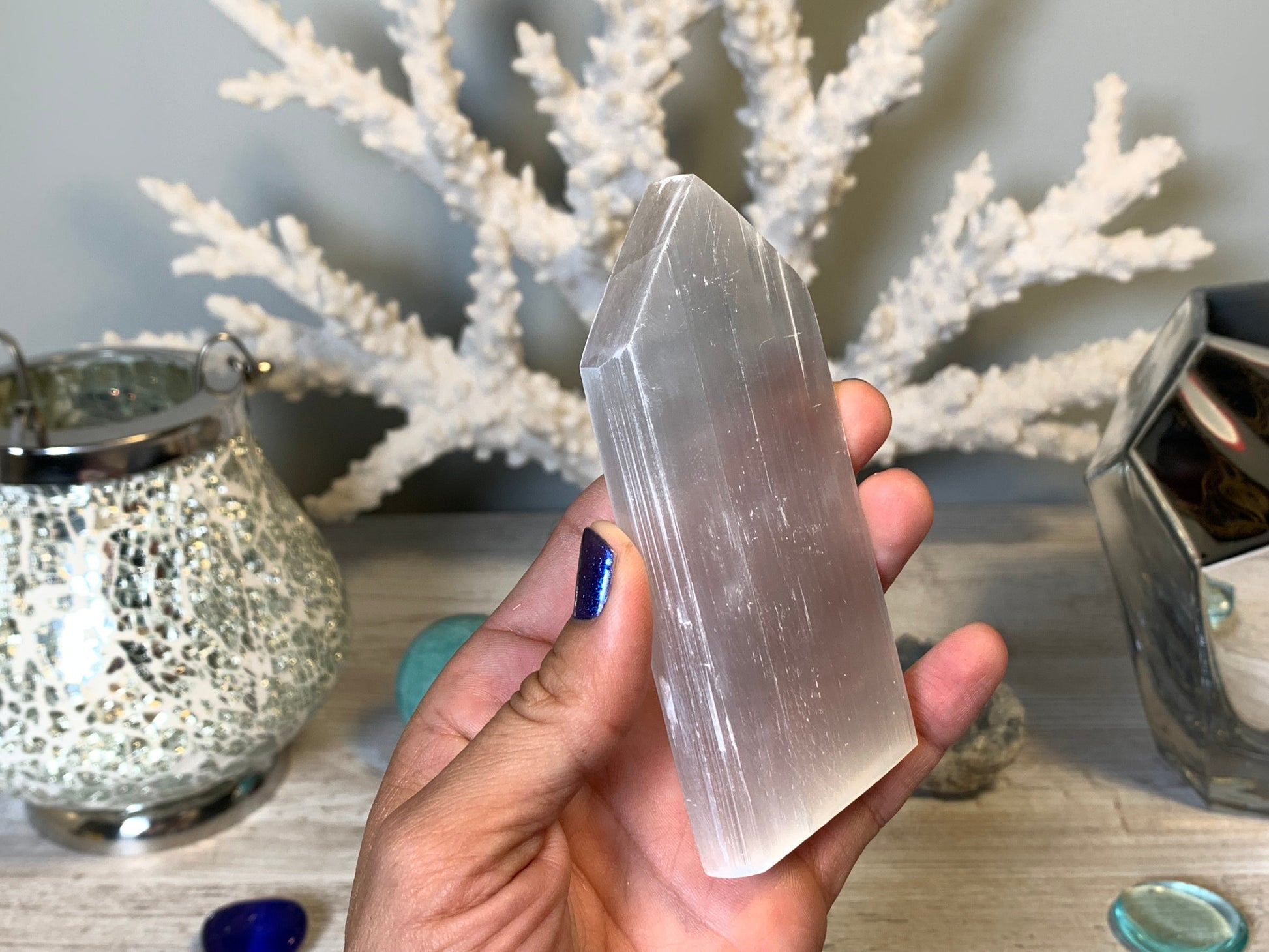hand holding Selenite Flat Point Crystals for energy and trust with white gray floral background.