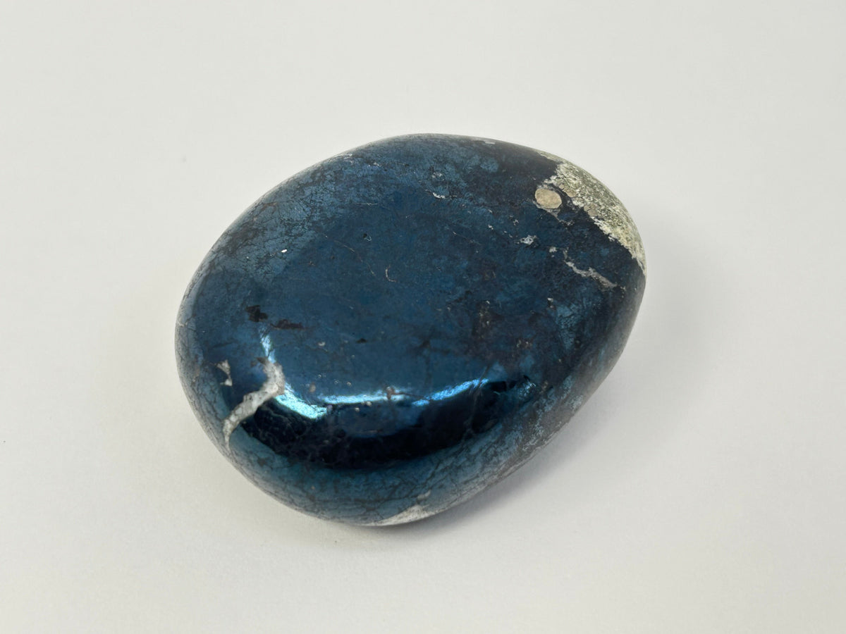 A polished dark blue Shimmering Covellite Healing Stone with natural white and gray crystalline inclusions, photographed on a neutral light gray background.