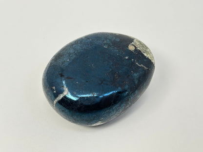 A polished dark blue Shimmering Covellite Healing Stone with natural white and gray crystalline inclusions, photographed on a neutral light gray background.