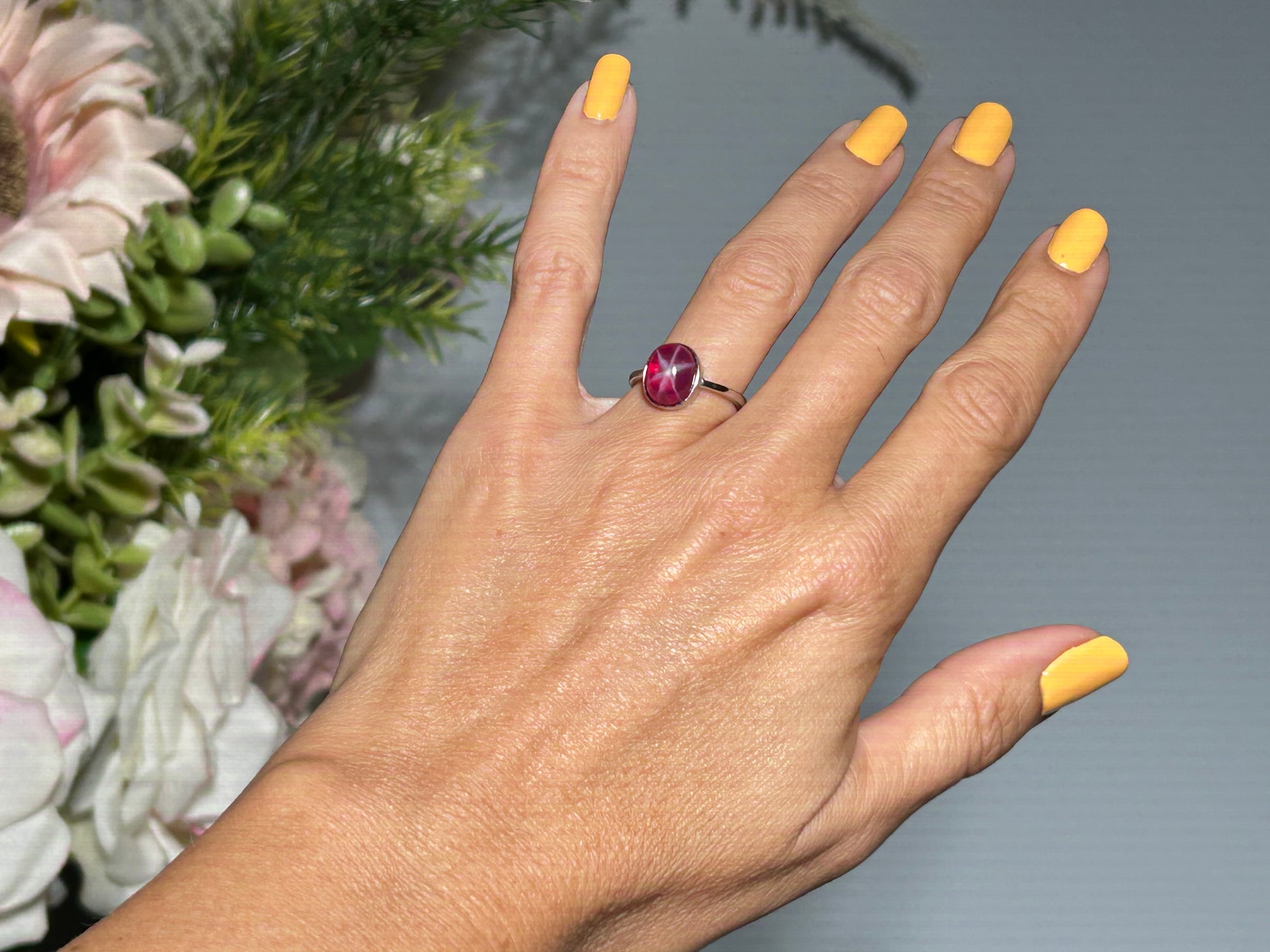 Hand wearing a Star Ruby Ring in Sterling Silver with gray and floral background.