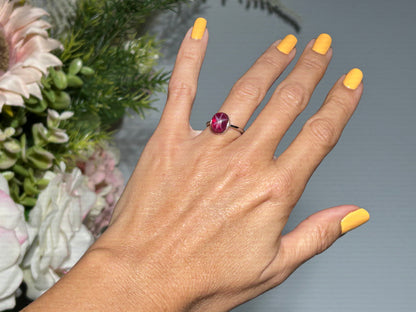 Hand wearing a Star Ruby Ring in Sterling Silver with gray and floral background.