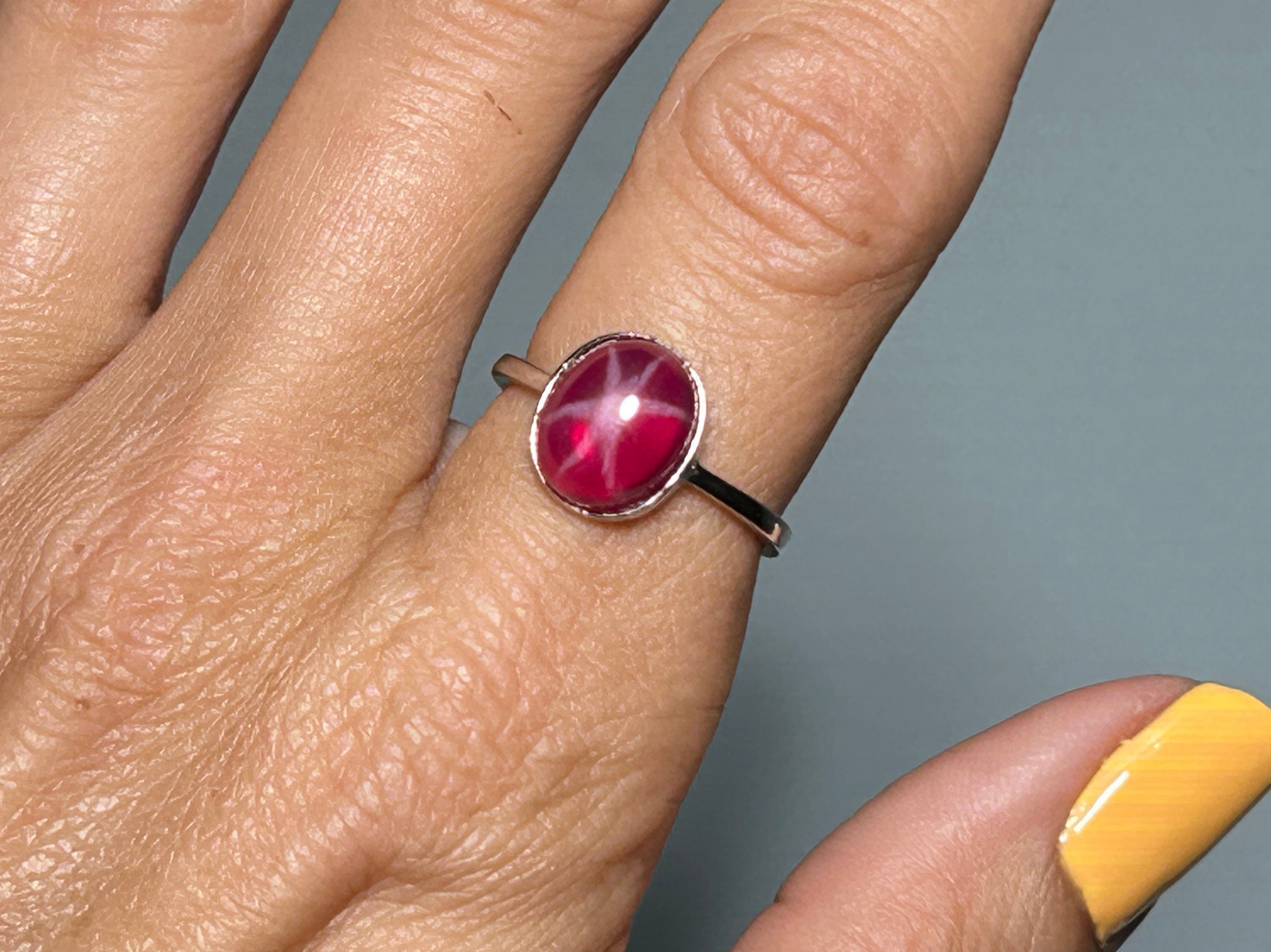 Close up of a finger wearing a Star Ruby and Sterling Silver Ring for meditation and energy work with gray background