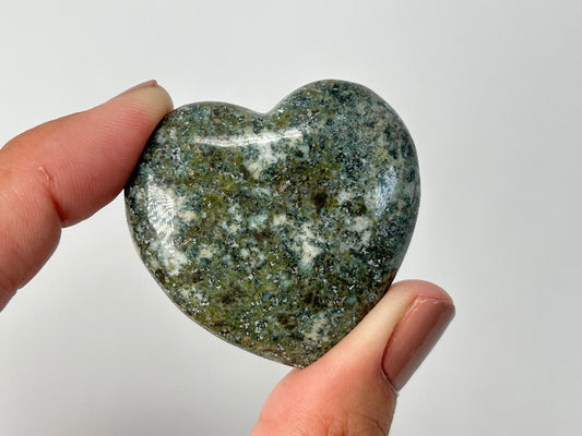 Heart-shaped Stonehenge Preseli Crystal held between fingers against a plain background