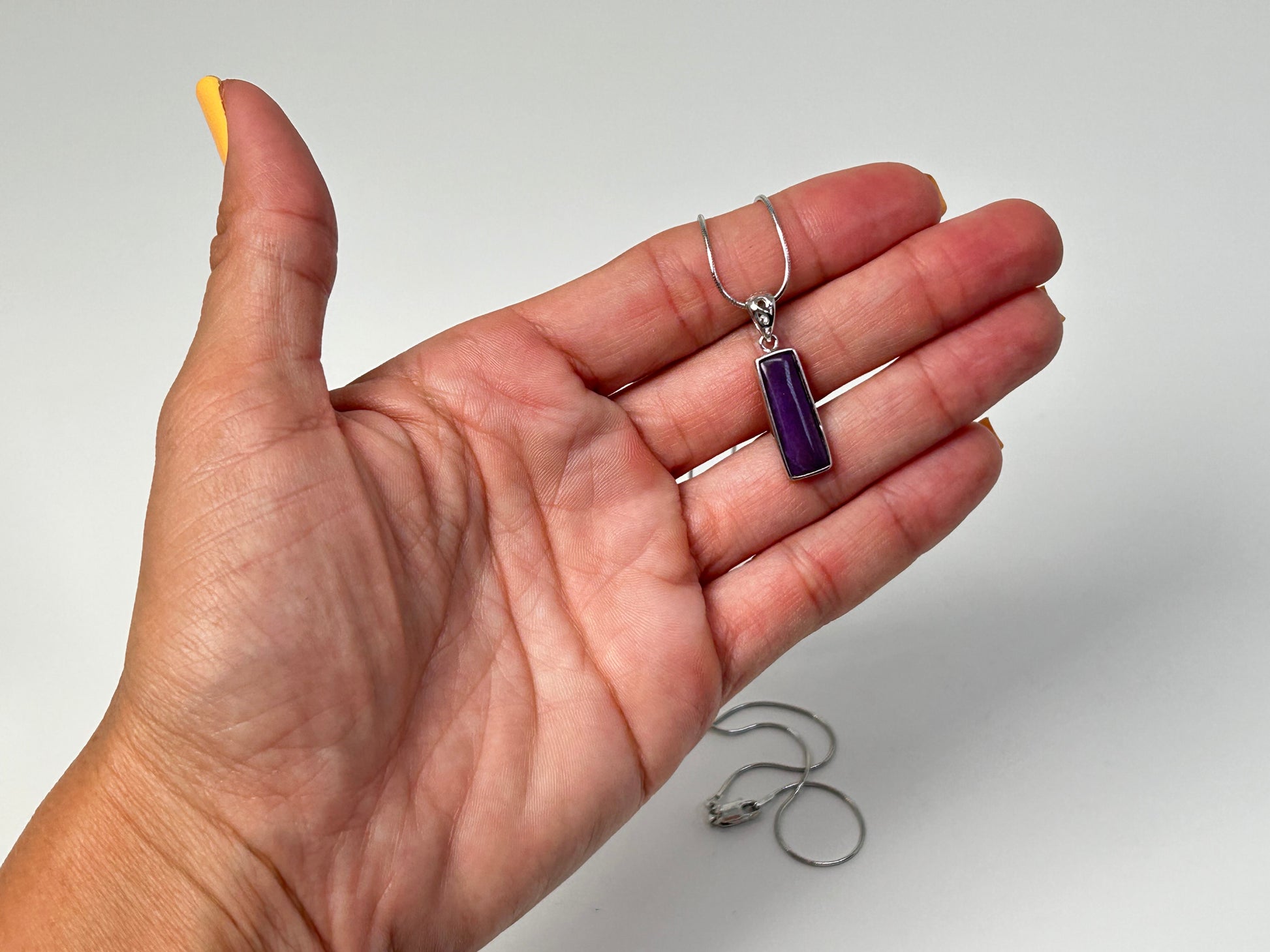 Hand holding a Sugilite Sterling Silver Pendant for meditation and energy work with white background