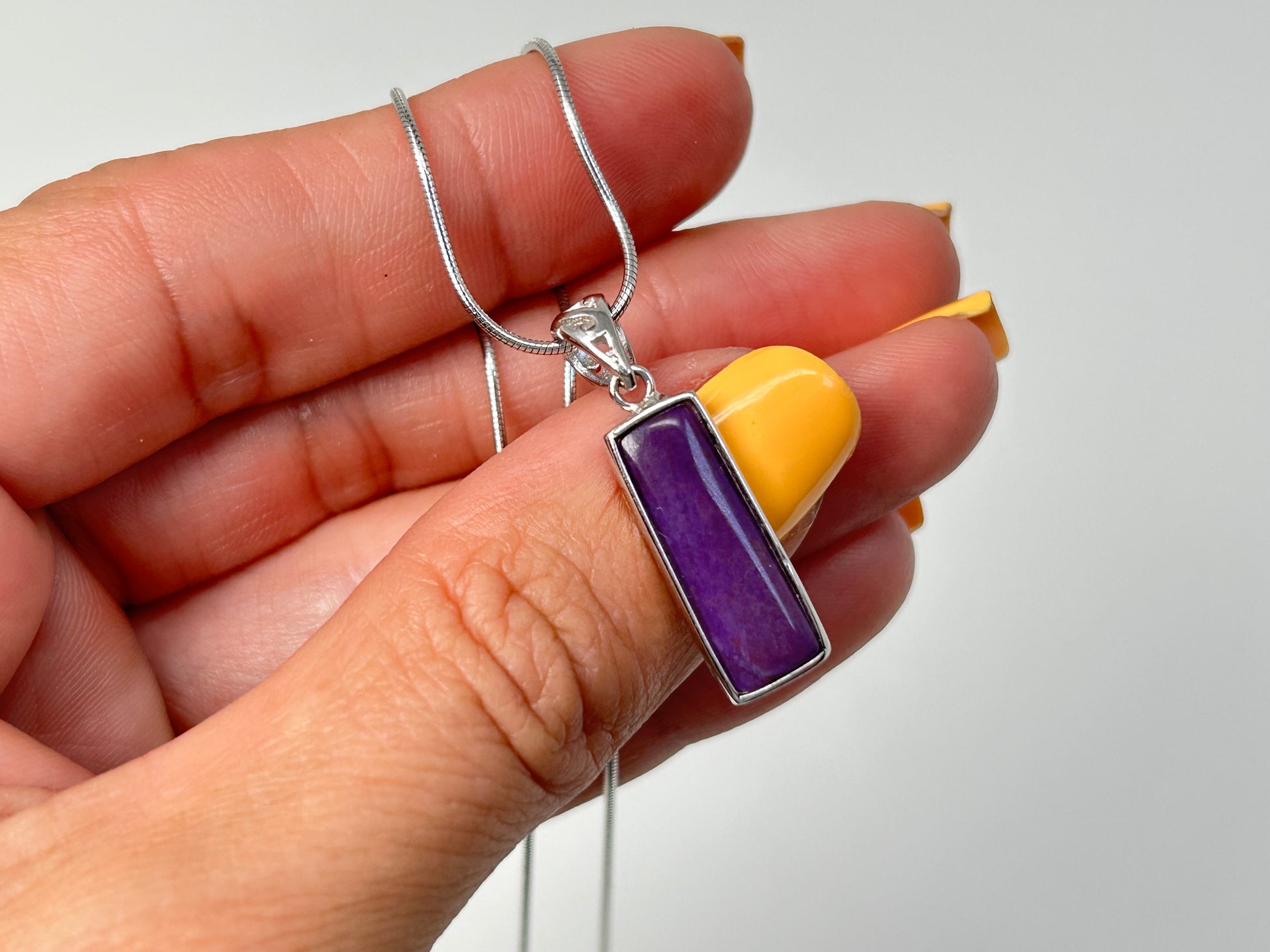 Close up of a Sugilite Sterling Silver Pendant on a silver chain against a white background.