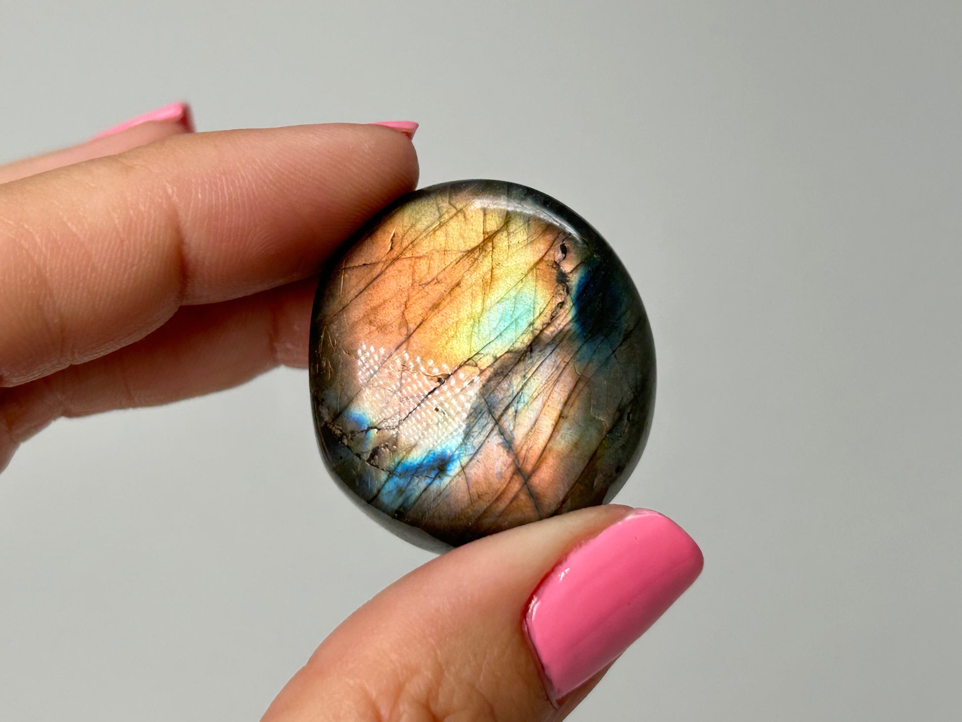 Hand holding a Labradorite stone with a gray background