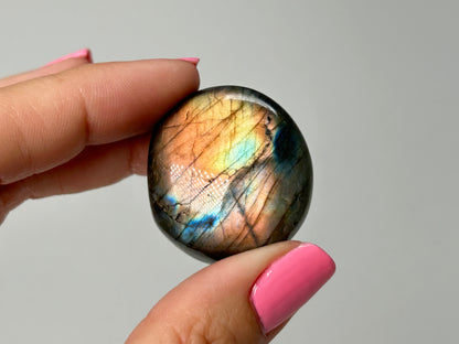Hand holding a Labradorite stone with a gray background
