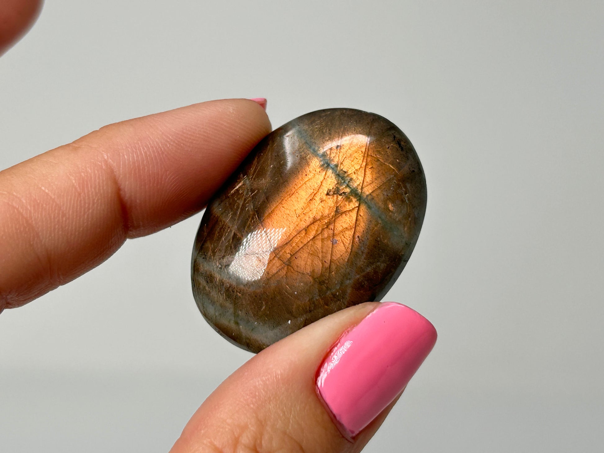 Hand holding a polished labradorite stone against a neutral background