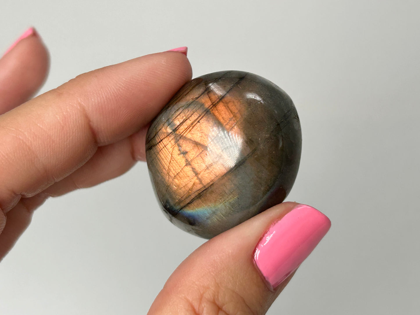 Hand holding a Labradorite stone with a reflective surface against a plain background