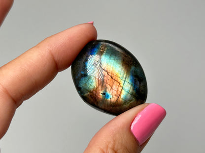 Person holding a colorful labradorite stone with a gray background