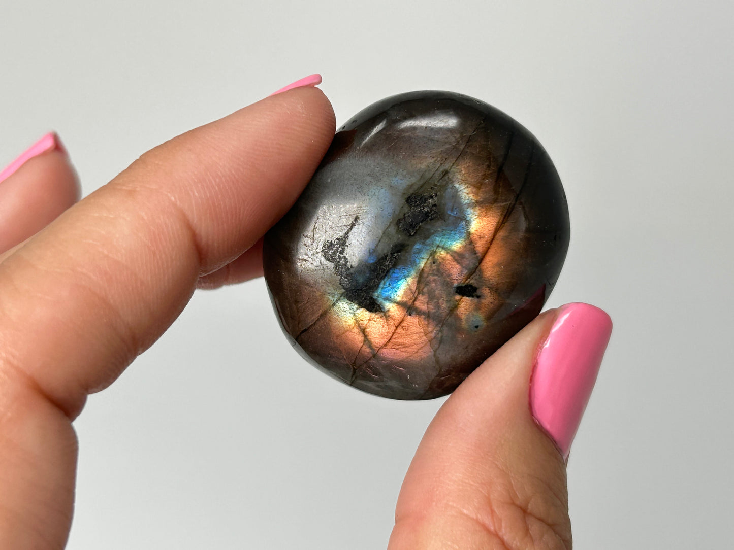 Person holding a shiny, multicolored labradorite stone against a neutral background