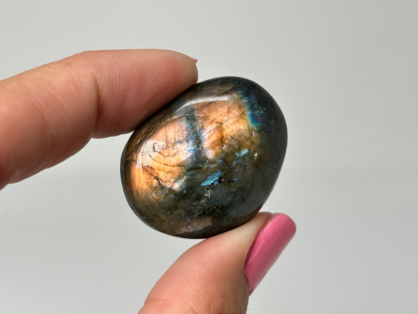 Hand holding a shiny, multicolored Labradorite stone against a plain background